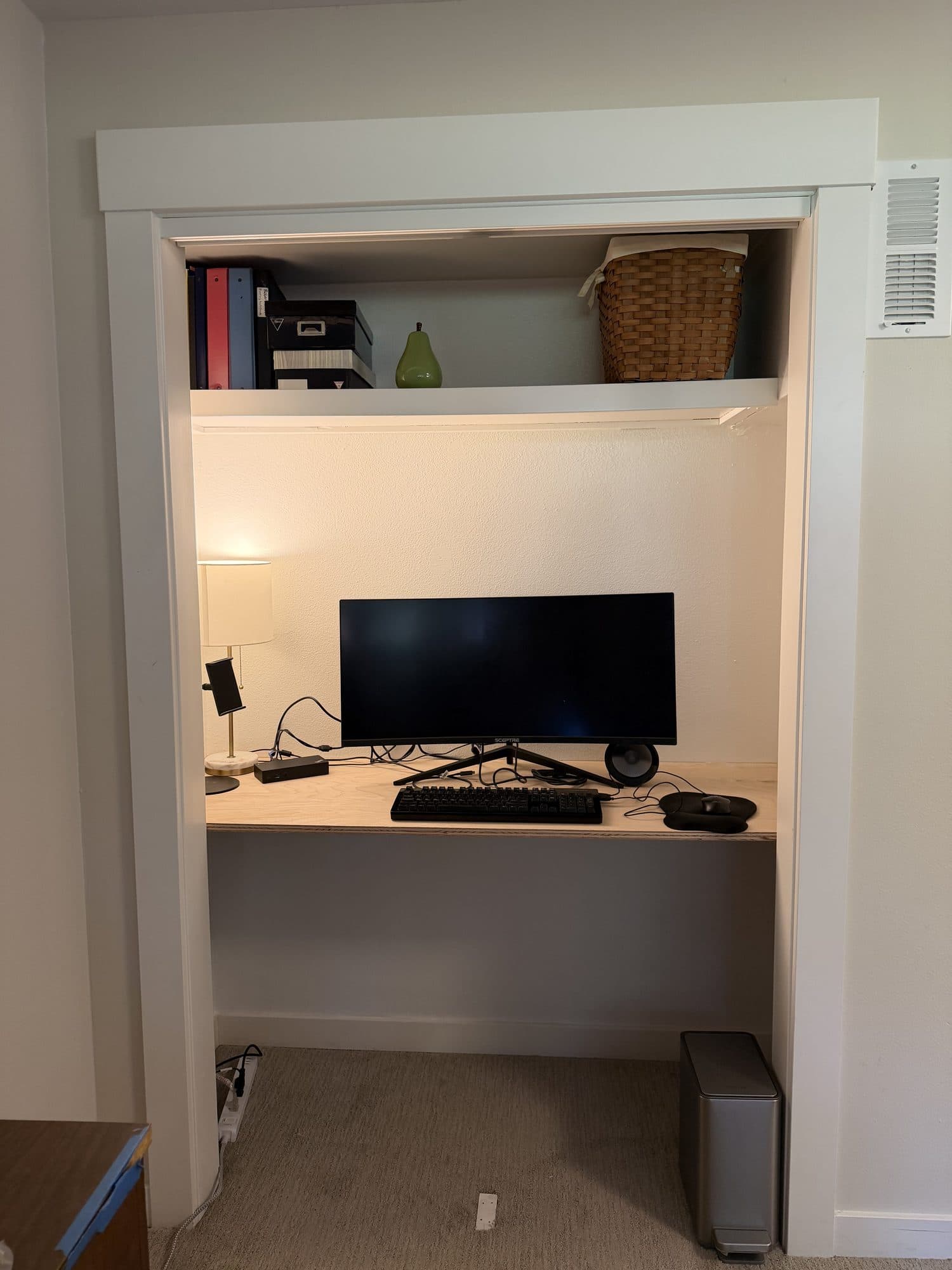 The finished closet desk with a monitor, lamp, and a shelf of books above